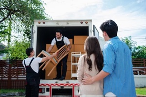 asian Couple check while unloading boxes and furniture from a pickup truck to a new house with service cargo two men movers worker in uniform lifting boxes