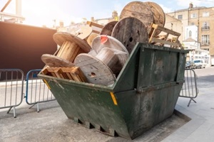 metal skip full of construction site rubbish and electric cable reels ready for collection in a street