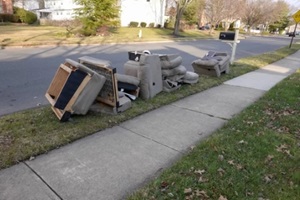 old disassembled chairs and cushions lined up by the curb waiting to be disposed of by the garbage men on trash day