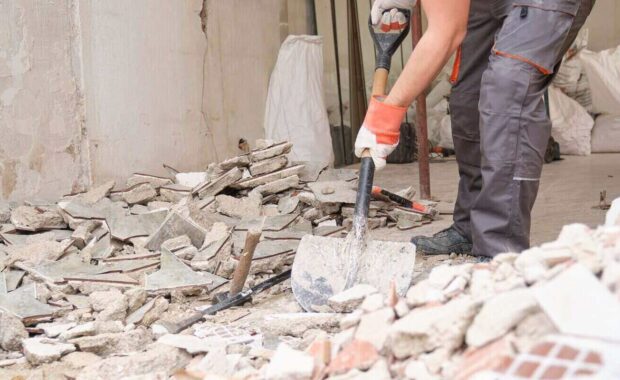 unrecognizable builder collecting construction debris with a shovel