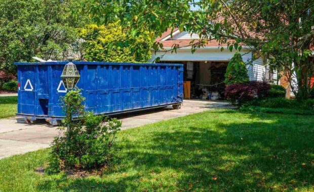 empty blue dumpster in the driveway of a house with its garage door open in a residential community